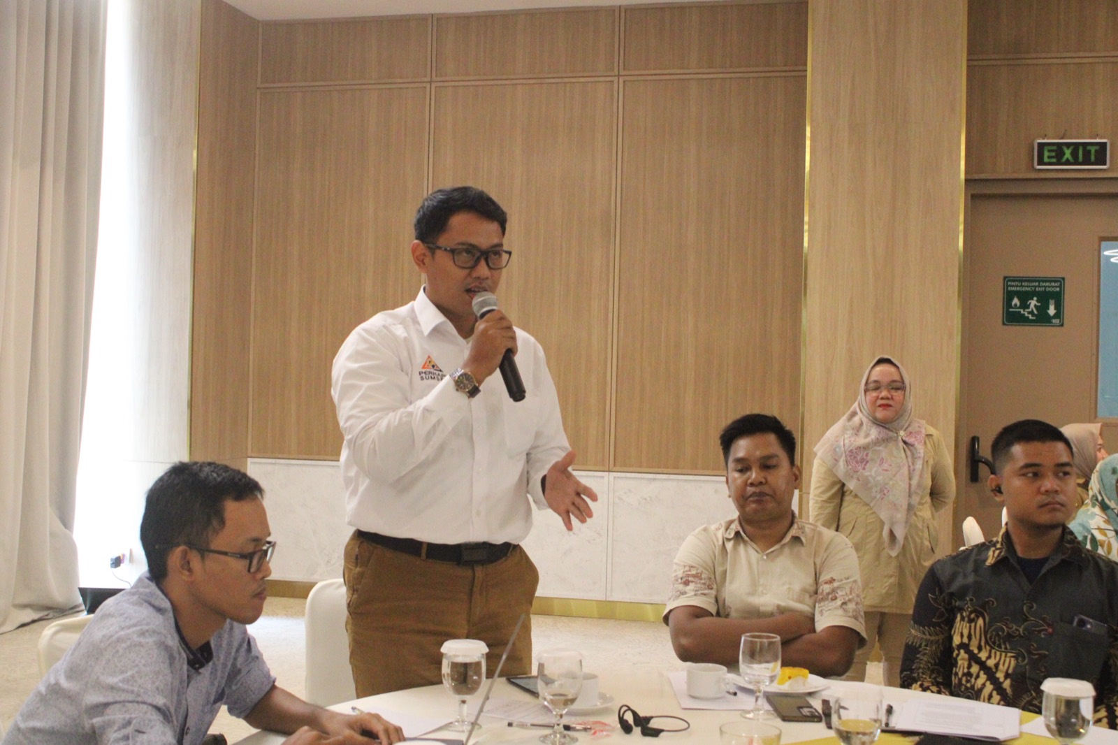 Participants seated around tables at a regional consultation forum in Palembang, one speaking into a microphone.